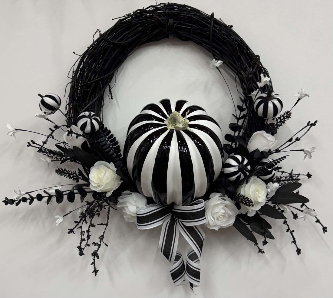 A glossy black-and-white striped pumpkin on a black grapevine ring with white roses, striped mini pumpkins, and a striped bow.