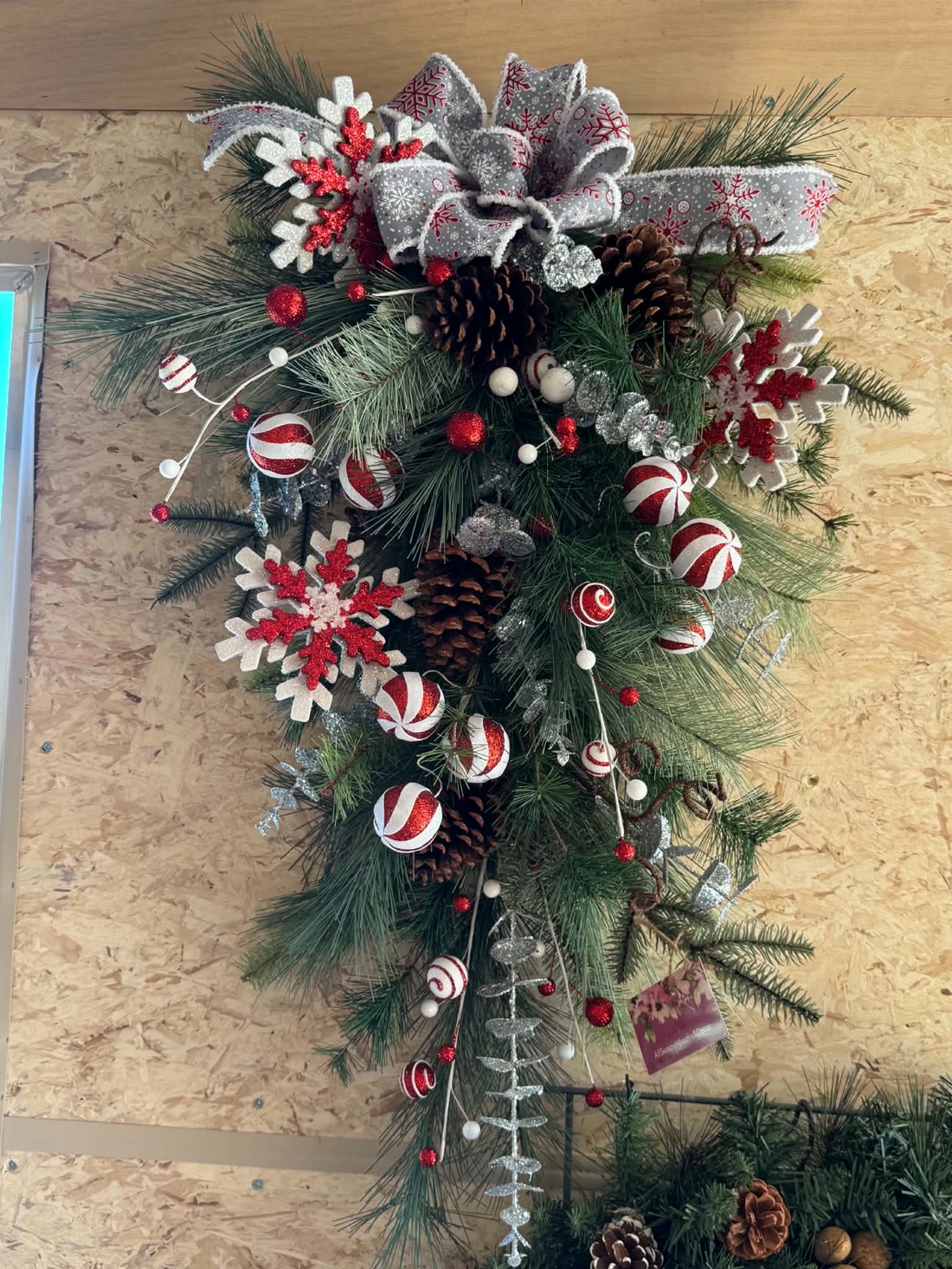A finished candy-cane swag: snowflake bow, striped ornaments, and pinecones over fresh pine.