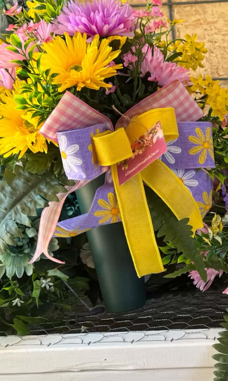 A cemetery spike arrangement in spring colors: pink, white, and yellow blooms on a tall spike stem.