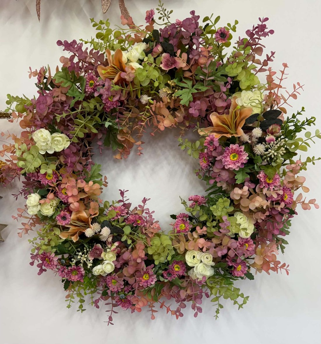 A full autumn wreath of mauve, blush, and green eucalyptus with cream ranunculus, orange lilies, and pink daisies.