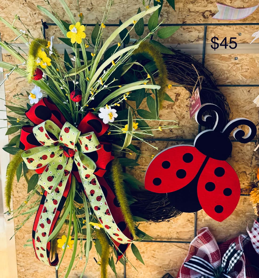 A summer garden wreath with a ladybug perched among red and white blooms and greenery.