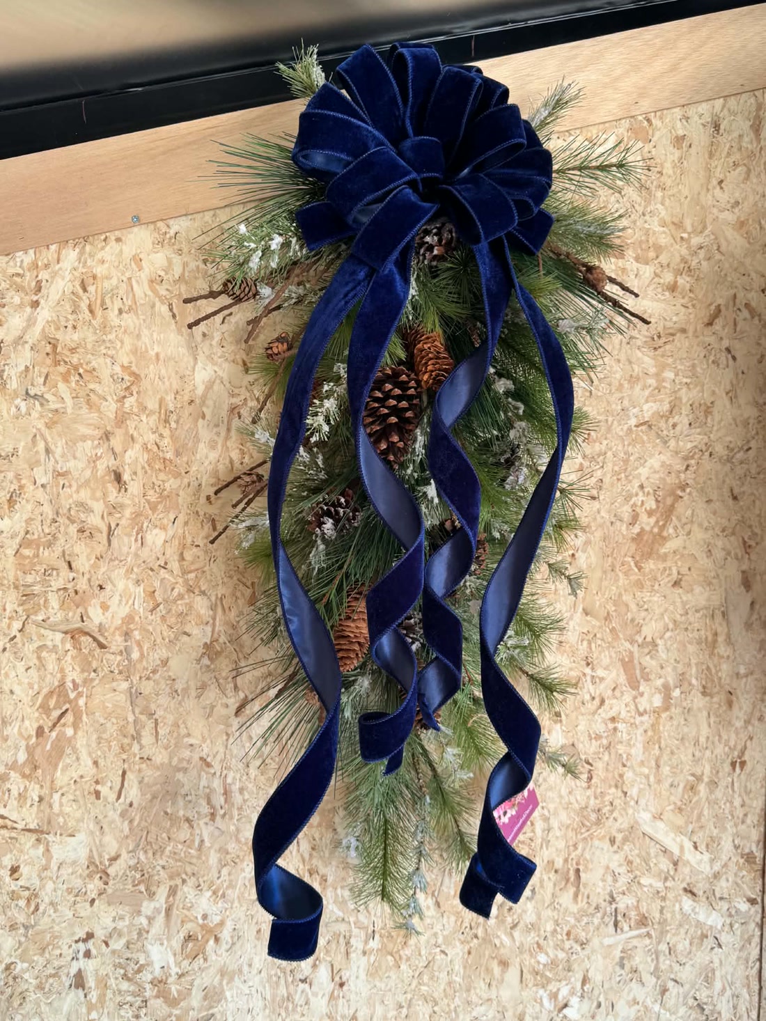 A navy velvet bow swag over snowy pine and pinecones, ribbons curling nearly to the floor.
