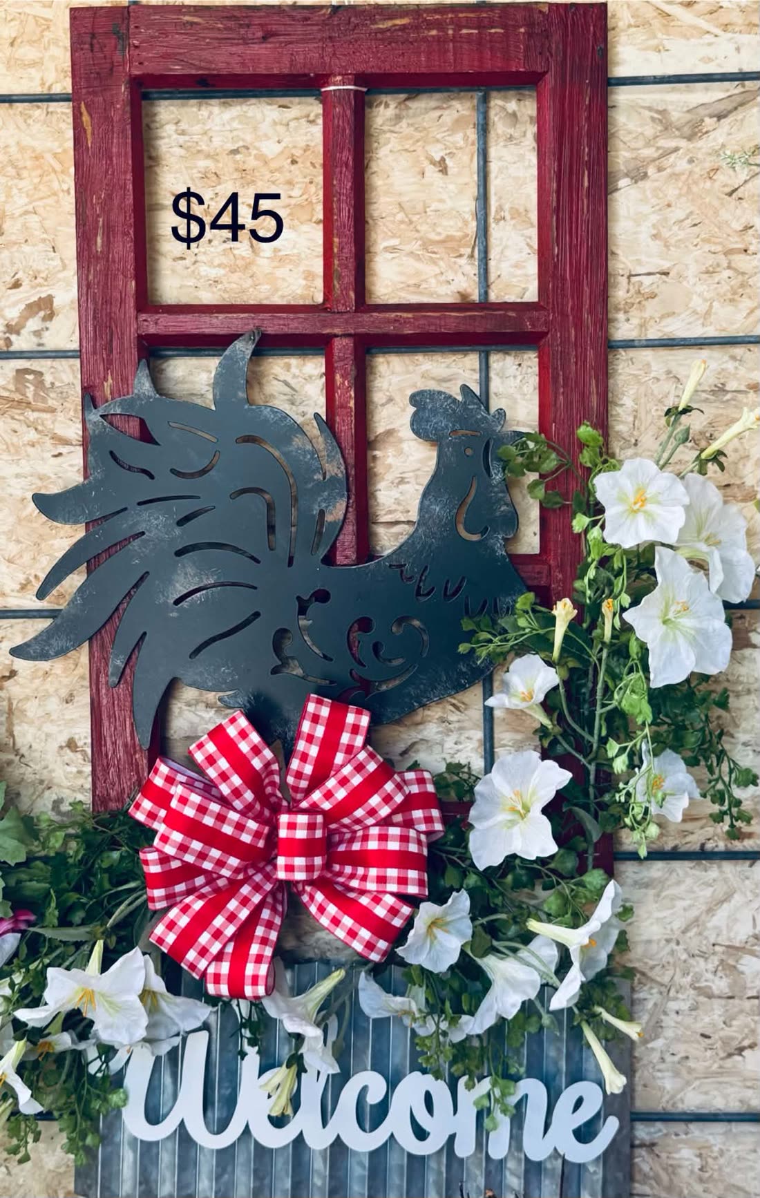 A barn-red window frame with a metal rooster, a big red gingham bow, and white petunias spilling from a Welcome planter box.