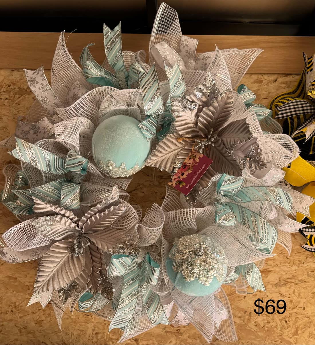 An evergreen Christmas wreath with teal poinsettias, silver sprays, and matching teal ribbon.